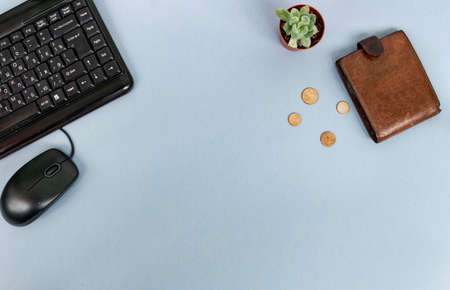 Unemployment concept. A lack of money. Coins fall out of a wallet on a gray background with copy space. Nearby are books, a computer mouse, a keyboard and a succulent flowerの写真素材