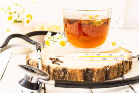 Decoction of chamomile, dried flower in flower tea and a phonendoscope, sliced lemon on a white wooden background. Health concept, prostate treatment, doctor prescribing treatment.の写真素材