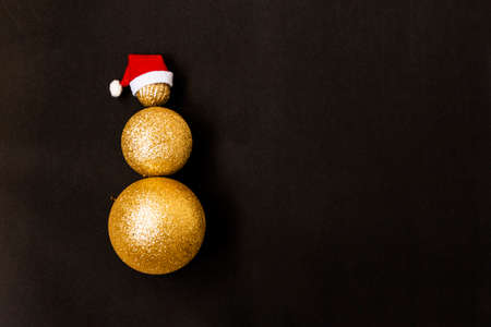 Christmas snowman made of golden Christmas balls of different sizes on a black background. Red santa...