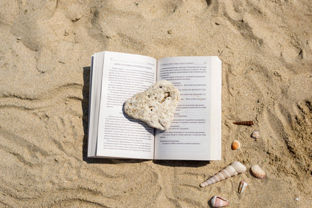 An open book crushed by a stone lies on the sand on the beach. Summer vacation on the beach.の写真素材