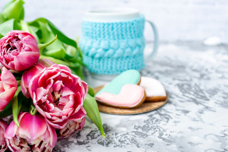 Bouquet of pink tulips, a cup of tea, and sweet gingerbread cookies in the shape of a heart on a light background. Copy space. Spring holiday concept, Valentine's Dayの写真素材