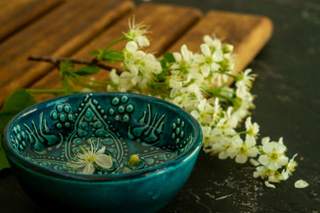 A blue oriental Turkish bowl with transparent water on a background of white cherry flowers on a wooden board and a black background. Copy space. Spring holiday conceptの写真素材