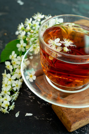 A transparent cup of teapot tea with a saucer and a white bird cherry flower on a black background. Copy space. Spring breakfast.の写真素材
