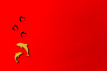 Two enamored dolphins, wooden fish with a crystal heart on a red background. Copy space. Valentine's day and weddingの写真素材