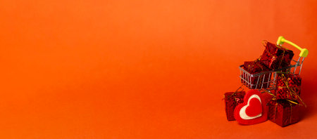 Shopping trolley with gift box, love hearts and space on red background. Valentine's Day buying and selling. Long bannerの写真素材