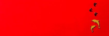 Two enamored dolphins, wooden fish with a crystal heart on a red background. Long banner valentine day. Valentine's Day and wedding concept.の写真素材