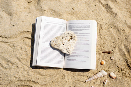 An open book crushed by a stone lies on the sand on the beach. Summer vacation on the beach.の写真素材