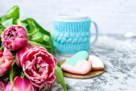 Bouquet of pink tulips, a cup of tea, and sweet gingerbread cookies in the shape of a heart on a light background. Copy space. Spring holiday concept, Valentine's Dayの写真素材