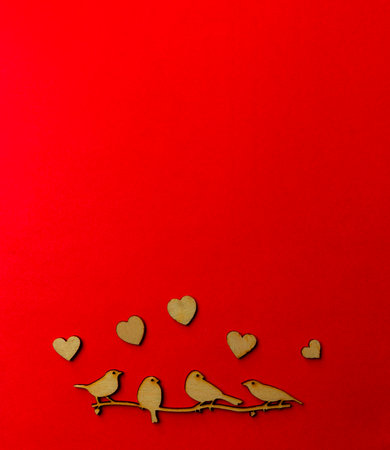 Wooden decoration flock of enamored birds sitting on a branch and wooden hearts around birds on a red background. Copy space. Valentine's day and weddingの写真素材