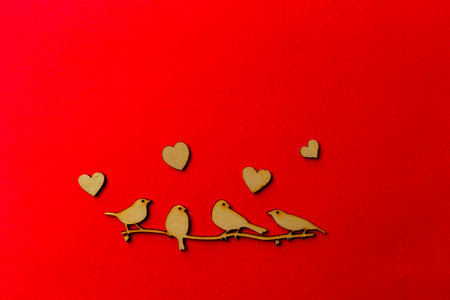Wooden decoration flock of enamored birds sitting on a branch and wooden hearts around birds on a red background. Copy space. Valentine's day and weddingの写真素材
