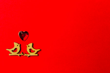 Two wooden birds in love sitting on a branch and hearts on a red background. Copy space. Valentine's day and weddingの写真素材