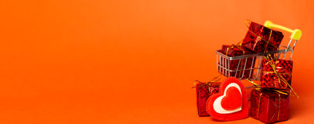 Shopping trolley with gift box, love hearts and space on red background. Valentine's Day buying and selling. Long bannerの写真素材