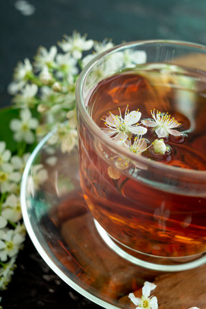 A transparent cup of teapot tea with a saucer and a white bird cherry flower on a black background. Copy space. Spring breakfast.の写真素材