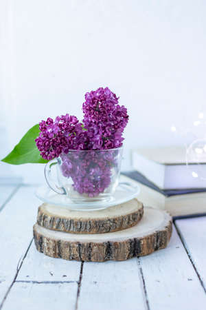 Transparent cup with flowers. Beautiful lilac fills the glass. The spring bouquet is worth no wooden cuts. Macro image of spring lilac purple flowers. Book in the background and lights. Blurredの写真素材