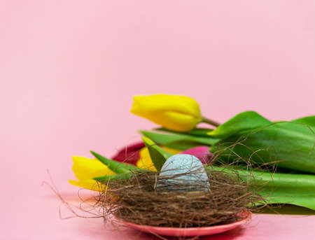 Spring postcard. Easter eggs in a nest with moss and a bouquet of fresh tulips on a pink background. Easter concept. Flat top view copy space. Spring flowers tulips.の写真素材