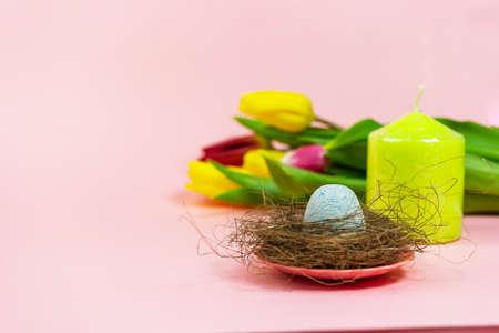 Spring postcard. Easter eggs in a nest with moss and a bouquet of fresh tulips, green candle on a pink background. Easter concept. Flat top view copy space. Spring flowers tulips.の写真素材