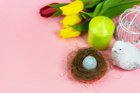 Spring postcard. Easter eggs in a nest with moss, a bird, a cage and a bouquet of fresh tulips, a green candle on a pink background. Easter concept. Flat top view copy space. Spring flowers tulipsの写真素材