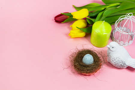 Spring postcard. Easter eggs in a nest with moss, a bird, a cage and a bouquet of fresh tulips, a green candle on a pink background. Easter concept. Flat top view copy space. Spring flowers tulipsの写真素材