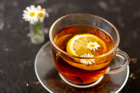 chamomile tea with lemon in a transparent cup on a black background. Breakfast concept, herbal tea.の写真素材