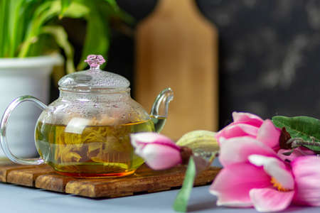 green tea with rose petals in a transparent teapot on a wooden table on a black background. The background is blurred. Tea drinking.の写真素材