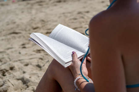 Woman reading a book on the beach, blurred background. Summer leisure on the beach.の写真素材