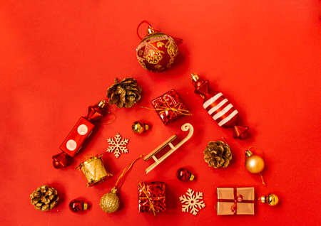 Flat composition with a Christmas tree made of different festive items, snowflakes, gifts, sweets, Christmas tree decorations on a red background. Copy spaceの写真素材