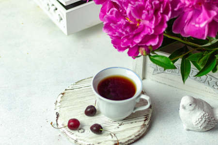 Shabby chic tea. A cup of tea on a white wooden tray with a cherry nearby. Peonies are in a white box. Blurred background.の写真素材