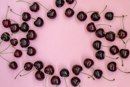 Red cherries on a pink background in the form of a round frame. Cherry background. Sweet cherry isolated on pink background cutout. Copy spaceの写真素材