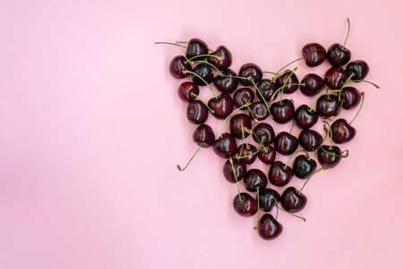 Heart shaped red cherries on a pink background. Cherry background. Sweet cherry isolated on pink background cutout. Copy space.の写真素材