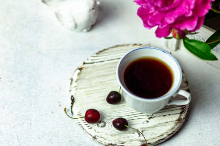 Shabby chic tea. A cup of tea on a white wooden tray with a cherry nearby. Peonies are in a white...