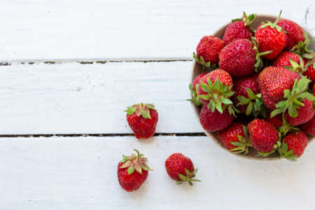 Ripe red strawberries lie in a white cup on a wooden white table. Copy space. View from above.の写真素材