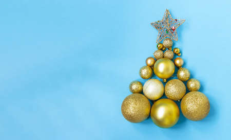Creative Christmas tree made of gold baubles and a star on a blue background, copy space. Minimal, new year concept. top view, flat lay.の写真素材