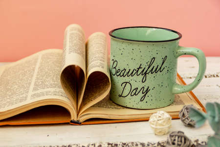 A green cup of tea stands on a book. Pink background. Eucalyptus flowers. The pages of the book are wrapped in the shape of a heart.の写真素材