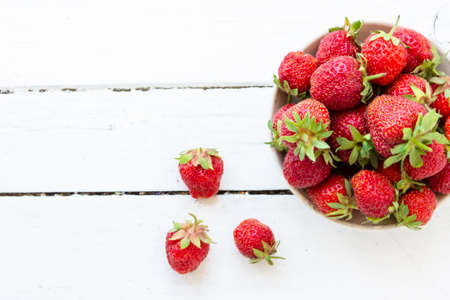 Ripe red strawberries lie in a white cup on a wooden white table. Copy space. View from aboveの写真素材