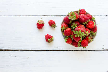 Ripe red strawberries lie in a white cup on a wooden white table. Copy space. View from aboveの写真素材
