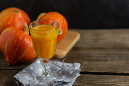 Pumpkin smoothie, spicy latte in a glass. In the background in blur orange pumpkins on a wooden vintage background. Copy space. Cozy table in hygge style.の写真素材