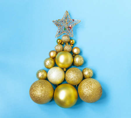 Creative Christmas tree made of gold baubles and a star on a blue background, copy space. Minimal, new year concept. top view, flat layの写真素材