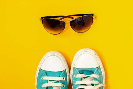Sunglasses, turquoise sneakers with white laces and rubber soles on a bright yellow background. stylish filling of clothes. selective focus, copy space, bannerの写真素材