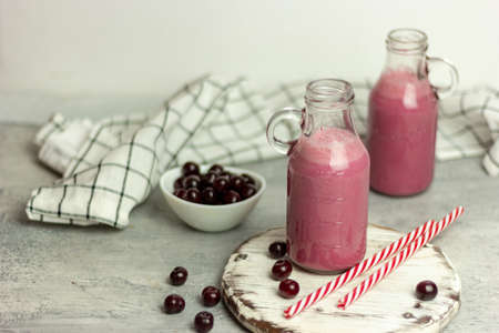 A bottle of cherry smoothies on a white background, cherries in bulk and in a plate. Morning summer breakfastの写真素材