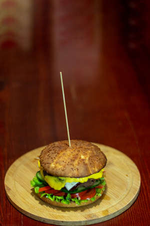 Burger from a meat patty with fresh cucumbers, tomatoes and cheese. White bun sprinkled with sesame seeds. close-up.の写真素材