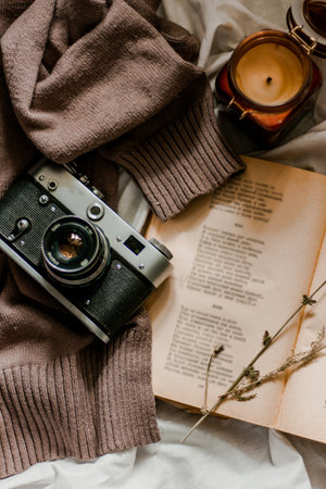 Vintage film camera with an old book wrapped in a warm knitted sweater and an extinguished candle...
