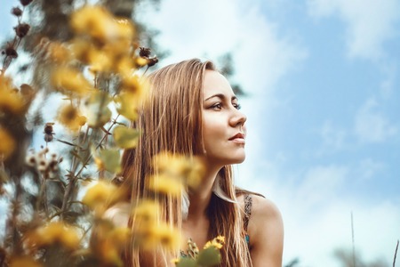 Portrait of a beautiful young girl contemplating among yellow flowers and clouds.の写真素材