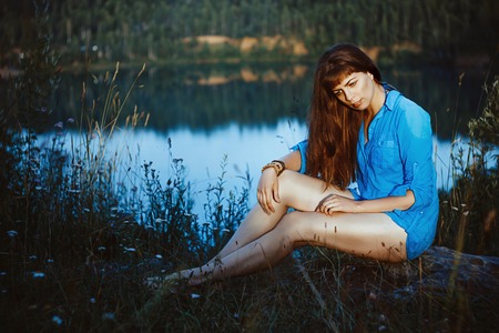A girl sits on the shore of the lake with bare feet and disheveled hairの写真素材
