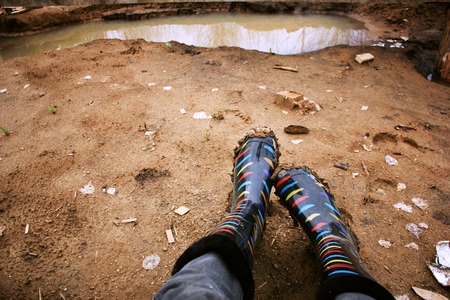 Legs in colored rubber boots soiled with clay, amid puddles.の写真素材