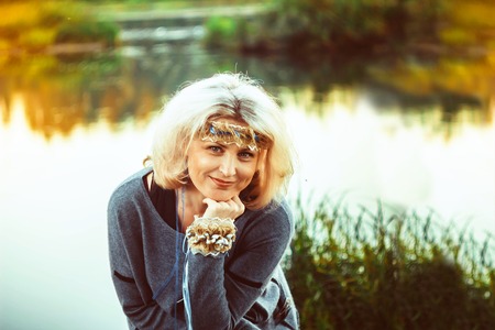 Beautiful mature woman standing in front of the river in autumnの写真素材