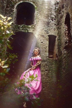 Beautiful young woman with long hair braided in a braid sitting in the window of the tower.の写真素材