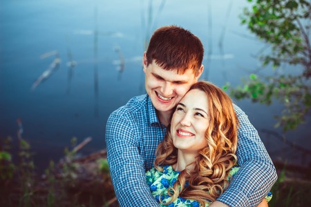 Loving couple in an embrace laughing while sitting by the lake.の写真素材