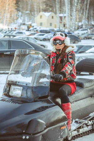 Beautiful girl sitting on a snowmobile in the winter forestの写真素材