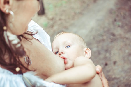 The mother feeds the young baby in the countryside in the sunlight at sunset. Breast feeding.の写真素材