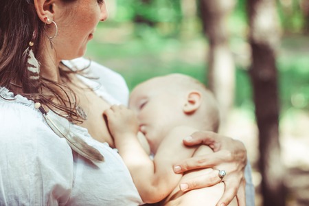 The mother feeds the young baby in the countryside in the sunlight at sunset. Breast feeding.の写真素材